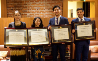 Four young adults hold up framed diplomas.