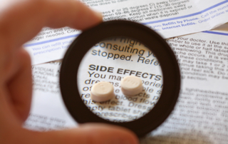 A small magnifying glass shows a couple of pills on a sheet of paper reading, Side Effects