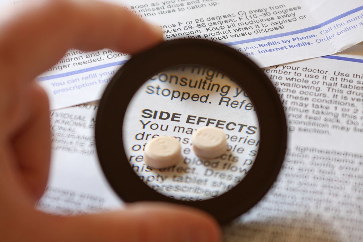A magnifying glass focuses on two pills resting on a page that reads Side Effects