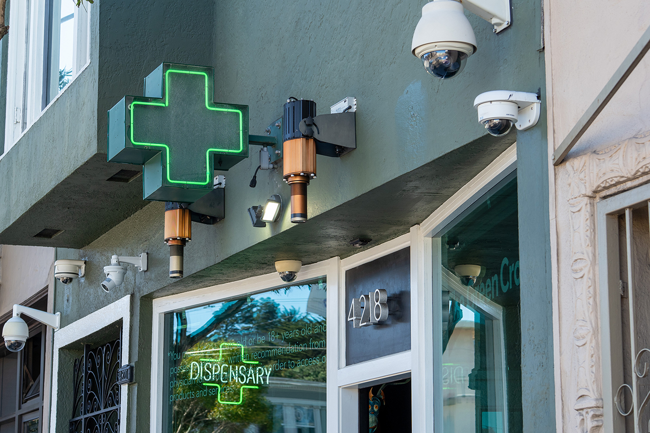 An illuminated green cross marks a storefront dispensary