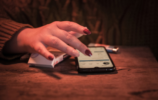 A woman's hand rests on a pack of cigarettes as she taps a smartphone