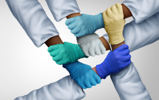 Several hands from different races, clad in white sleeves and latex gloves, clasp each others' wrists
