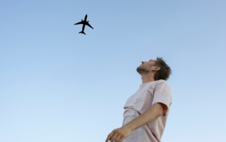 A shabbily dressed man watches an airport flying overhead.