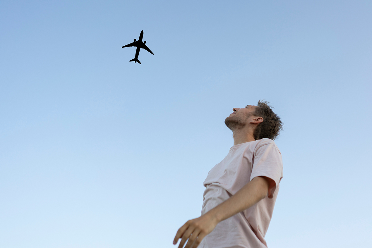A haggard man watches a passenger jet fly overhead