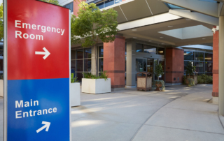 A hospital entrance sign uses arrows to guide new arrivals to the emergency room and the main entrance