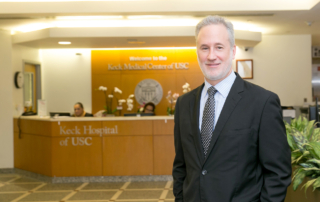 A businessman with a silver beard stands in front of a Keck Medicine reception desk