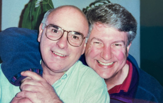 Two older men huddle close as they beam at the camera