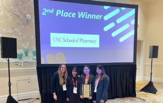 Four young women grin in front of an illuminated screen reading, second place winner, USC School of Pharmacy