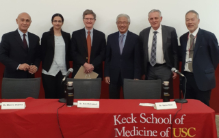 Six men in suits stand behind a table covered with a cloth reading, Keck School of Medicine of USC