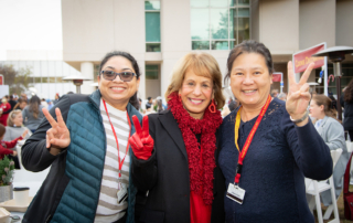 USC President Carol Folt raises USC's V for Victory hand gesture with two Health Sciences staff members