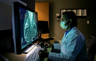 A man in a white coat and medical-grade mask analyzes a mammogram on a computer screen
