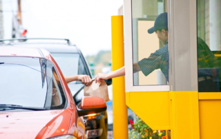 A fast food worker at a drive-thru window hands a bag to a customer in a car.