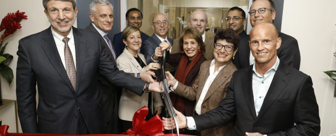 Eleven high-ranking professionals happily cut a red ribbon in front of a doorway with a sign reading, USC-CHLA Cell Therapy Program, CGMP Laboratory
