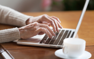 A closeup shows an older woman's hands typing on a laptop.