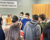 A group of teens listen to a man in scrubs in a cardiac rehab center
