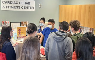 A group of teens listen to a man in scrubs in a cardiac rehab center