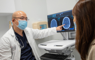 A masked doctor shows a brain scan to a patient