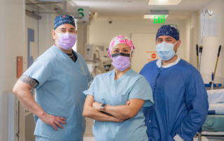 Three masked medical providers standing for a portrait in a hallway