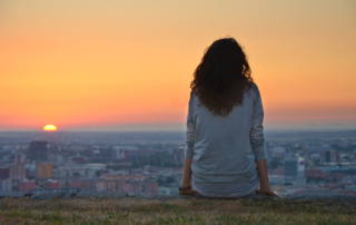 A young girl sits on a hill looking out over a city.