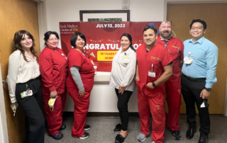 Seven members of the ECMO team smile in front of a congratulatory banner.