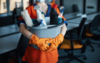 A woman in cleaning gloves and a stain-resistant apron holds a large bucket of cleaning supplies