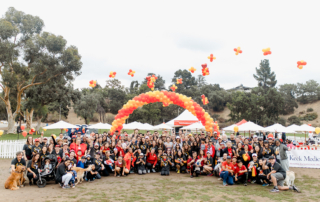 A large group of people in matching cardinal T-shirts pose for a photo in front of a ballon arch in cardinal and gold.