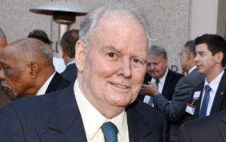 An older man in a suit smiles at an event