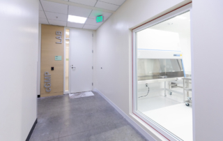 A hallway shows a large window to a lab on the right and a door reading cGMP lab at the end.