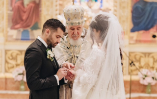 An older priest in an elaborate robe and hat marries a young, dark-haired couple.