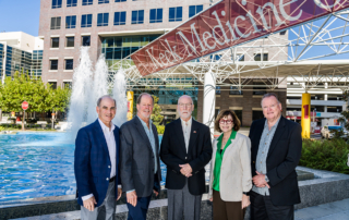 Former USC University Hospital executives stand in front of Keck Hospital of USC's fountain under a Keck Medicine banner