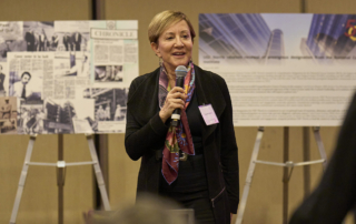 Caryn Lerman speaks in front of two collages depicting the history of USC Norris