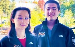 Two smiling scientists wear fleece jackets embroidered with the Rong Lu Lab logo.