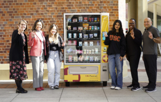 Six people surrounding a vending machine smile proudly.