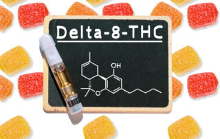 Gummy candies surround a vape cartridge that lies on a chalkboard which reads Delta-8-THC