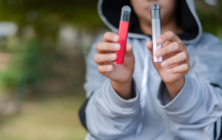 A teen holds two vaping products: one for cannabis and the other an e-cigarette